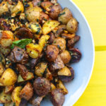 Roasted crunchy baby potatoes cut in quarters, served on white plate on yellow backdrop