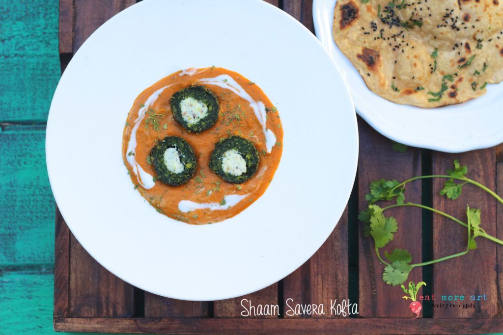 An overhead shot of plate of green spinach kofta with cut in half with white panner in center in orange color gravy served with a side of roti with teal color pool background